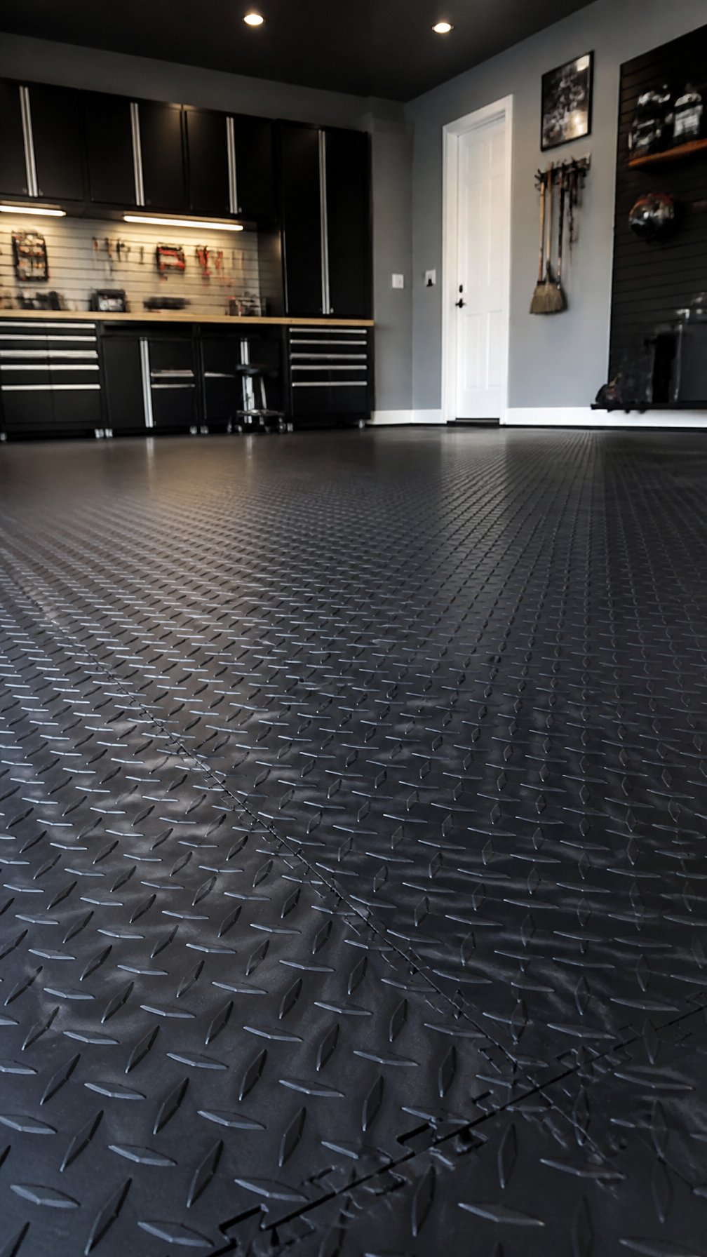 A garage floor covered with black interlocking diamond-patterned tiles in a clean and organized workspace.